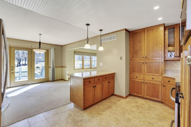 kitchen featuring visible vents, a peninsula, light countertops, pendant lighting, and brown cabinets