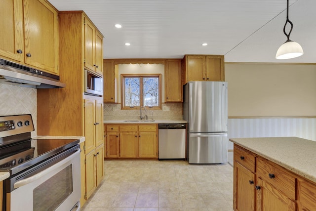 kitchen with under cabinet range hood, decorative light fixtures, wainscoting, appliances with stainless steel finishes, and a sink