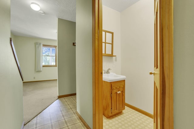 hallway featuring a sink, baseboards, and light floors