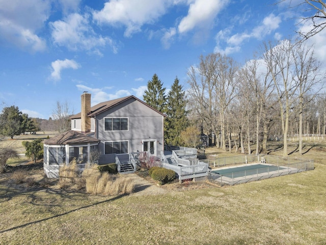 rear view of house featuring a wooden deck, a yard, a sunroom, and a chimney