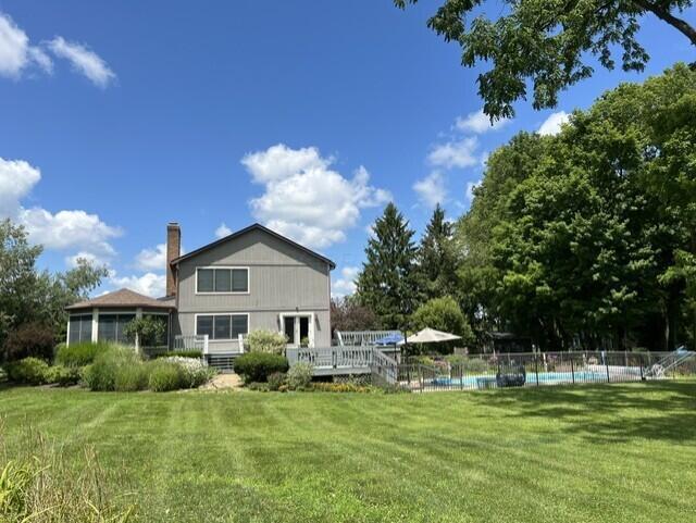 rear view of property featuring fence, a fenced in pool, a wooden deck, a yard, and a chimney