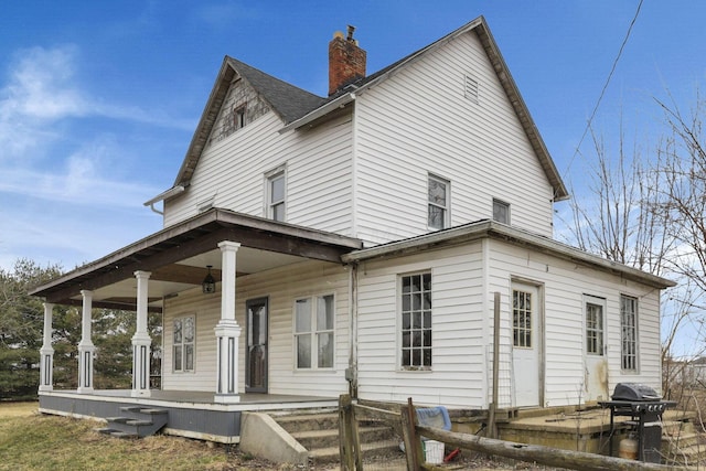 rear view of house with roof with shingles, a porch, and a chimney