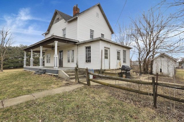 view of front facade featuring fence, roof with shingles, covered porch, a chimney, and a front lawn