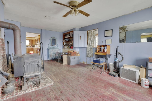 miscellaneous room featuring a ceiling fan, a wood stove, and hardwood / wood-style flooring