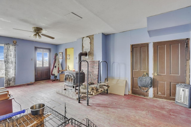 living area with a wood stove, wood finished floors, and ceiling fan