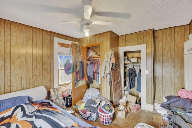 bedroom with wood walls, a textured ceiling, a ceiling fan, and wood finished floors