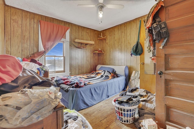 bedroom with a ceiling fan, wooden walls, and wood finished floors