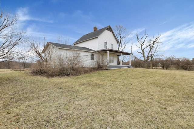 view of side of property with a lawn, covered porch, and a chimney