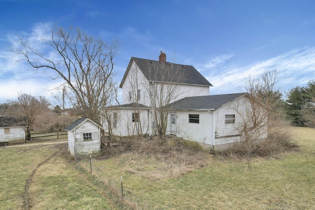 view of property exterior with fence, a chimney, a yard, an outbuilding, and a storage unit