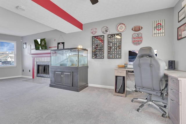 office featuring carpet flooring, baseboards, a ceiling fan, and a tiled fireplace