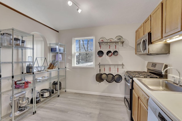 kitchen featuring light wood finished floors, arched walkways, appliances with stainless steel finishes, light countertops, and baseboards