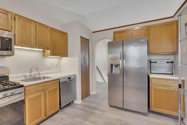 kitchen with lofted ceiling, a sink, stainless steel appliances, light countertops, and light wood-type flooring