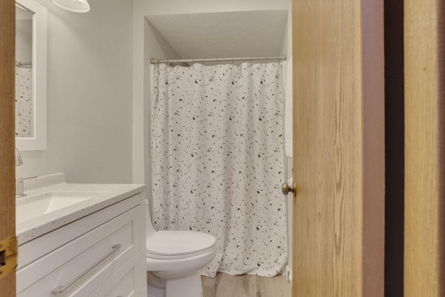 bathroom featuring toilet, vanity, a shower with shower curtain, wood finished floors, and a textured ceiling