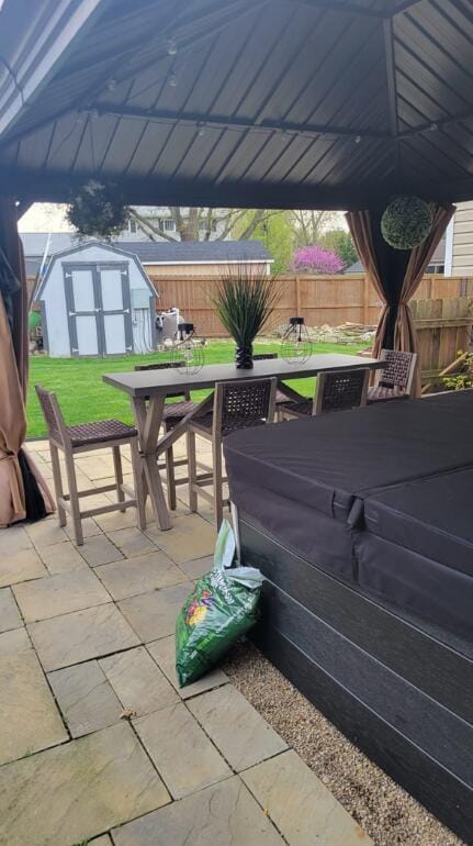 view of patio with an outbuilding, fence, a shed, outdoor dining area, and a hot tub