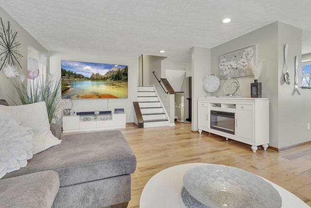 living room featuring light wood-style flooring, recessed lighting, stairs, a textured ceiling, and a glass covered fireplace