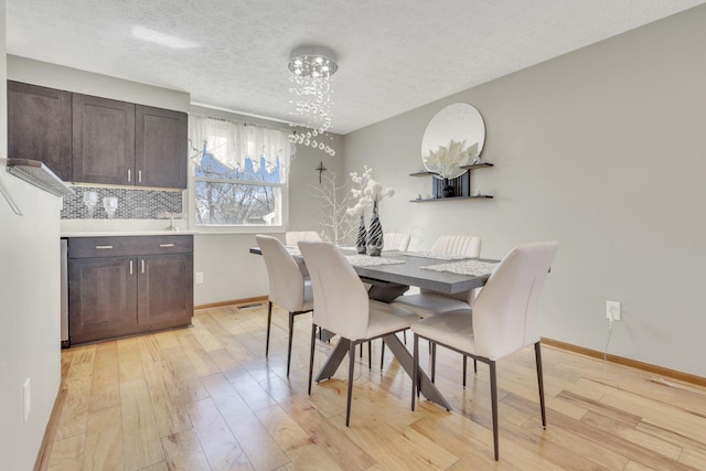 dining area featuring light wood finished floors, visible vents, baseboards, a notable chandelier, and a textured ceiling