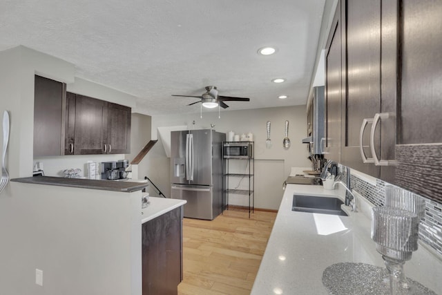 kitchen with light wood-type flooring, a ceiling fan, a sink, stainless steel appliances, and dark brown cabinetry