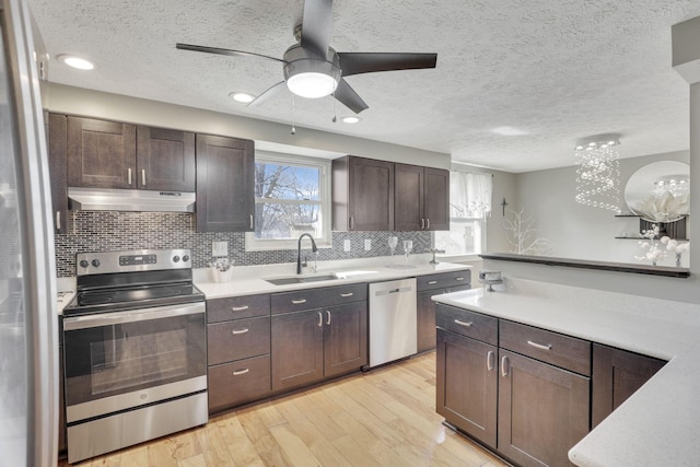 kitchen with a sink, under cabinet range hood, appliances with stainless steel finishes, light wood finished floors, and light countertops