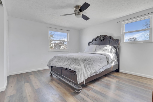 bedroom with ceiling fan, wood finished floors, baseboards, and a textured ceiling