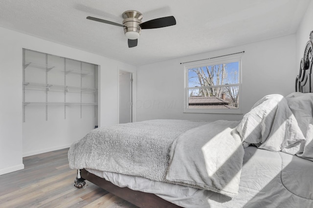 bedroom with wood finished floors, baseboards, ceiling fan, a closet, and a textured ceiling