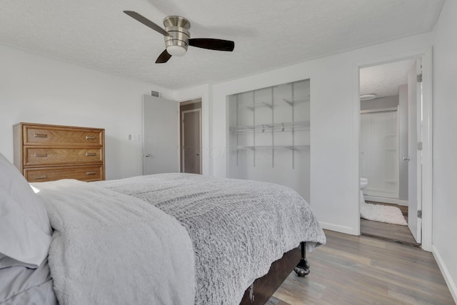 bedroom featuring a textured ceiling, ensuite bath, wood finished floors, baseboards, and ceiling fan