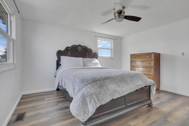 bedroom with a textured ceiling, wood finished floors, visible vents, and baseboards