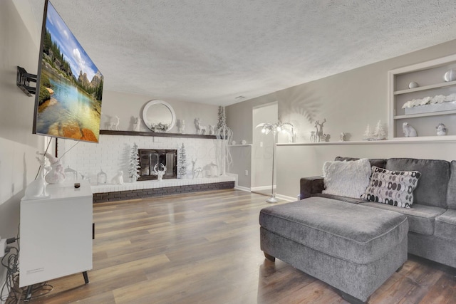 living area featuring built in shelves, a textured ceiling, wood finished floors, a fireplace, and baseboards