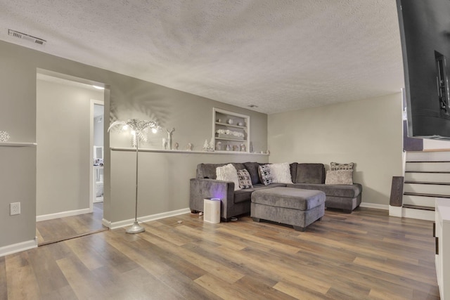 living area featuring visible vents, a textured ceiling, wood finished floors, baseboards, and stairs