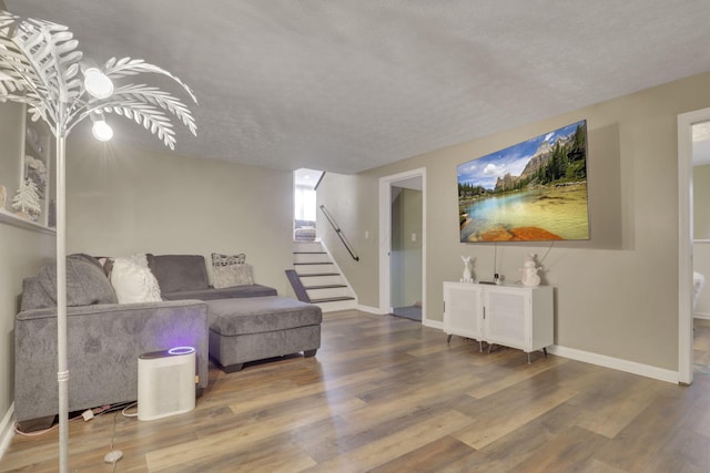 living room with stairway, wood finished floors, baseboards, and a textured ceiling