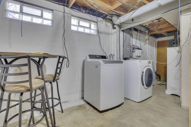 clothes washing area with electric panel, concrete block wall, laundry area, and washing machine and clothes dryer