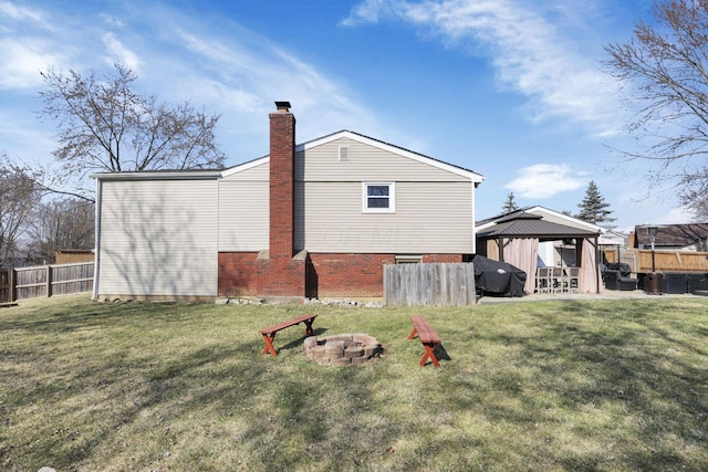 back of property featuring a gazebo, a fire pit, fence, and a lawn