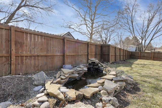 view of yard featuring a garden pond and a fenced backyard