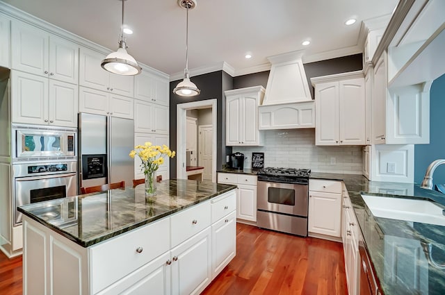 kitchen with appliances with stainless steel finishes, wood finished floors, custom exhaust hood, white cabinetry, and a sink