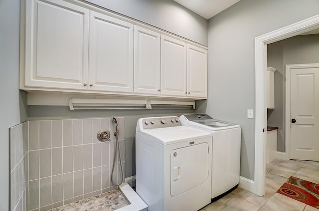 clothes washing area with washer and clothes dryer, cabinet space, and light tile patterned flooring