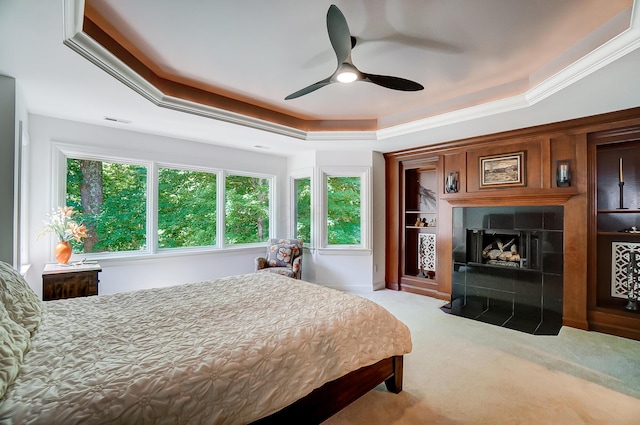 carpeted bedroom featuring ceiling fan, a raised ceiling, ornamental molding, and a tile fireplace