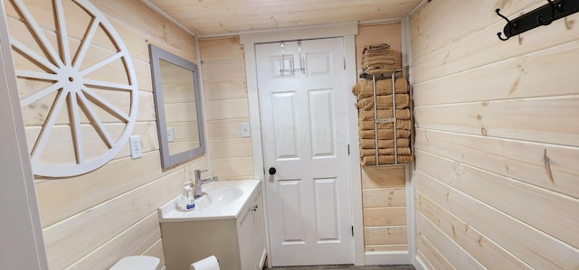 half bathroom featuring wood ceiling, wood walls, vanity, and toilet