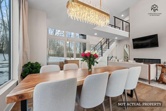 dining room with wood finished floors, a towering ceiling, recessed lighting, a chandelier, and stairs