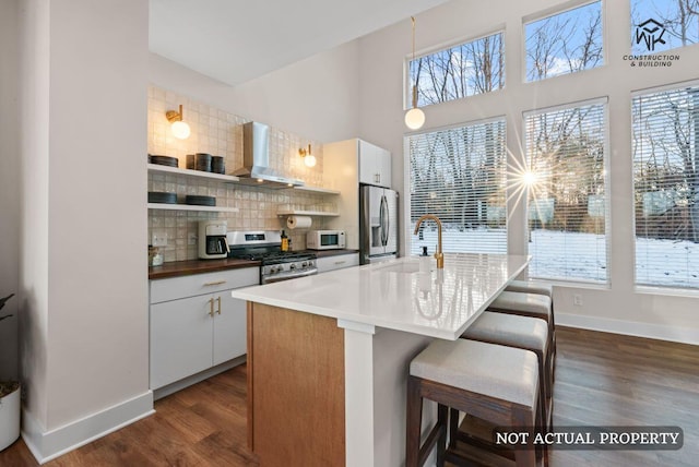 kitchen with a breakfast bar, dark wood-style flooring, stainless steel appliances, wall chimney exhaust hood, and backsplash