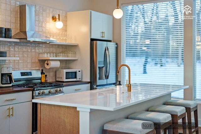 kitchen featuring open shelves, a sink, appliances with stainless steel finishes, wall chimney range hood, and a wealth of natural light