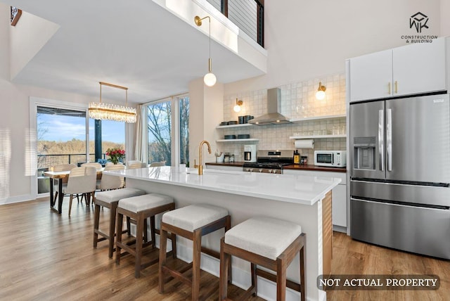 kitchen with tasteful backsplash, appliances with stainless steel finishes, a breakfast bar area, wall chimney exhaust hood, and light wood finished floors