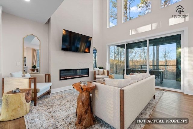 living area with a glass covered fireplace, a high ceiling, wood finished floors, and visible vents