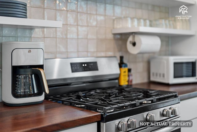 kitchen with white microwave, stainless steel range with gas stovetop, wooden counters, and tasteful backsplash