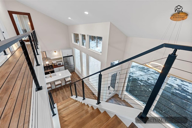 stairs with a notable chandelier, wood finished floors, recessed lighting, and high vaulted ceiling