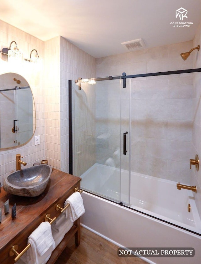 full bathroom with vanity, wood finished floors, visible vents, shower / bath combination with glass door, and tile walls