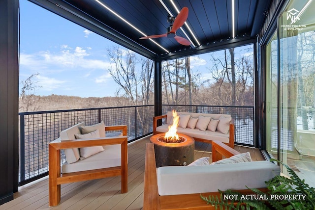 wooden terrace with a forest view, an outdoor living space with a fire pit, and a ceiling fan