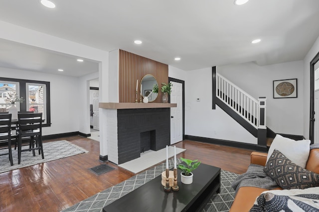 living area featuring wood finished floors, recessed lighting, stairway, baseboards, and a brick fireplace