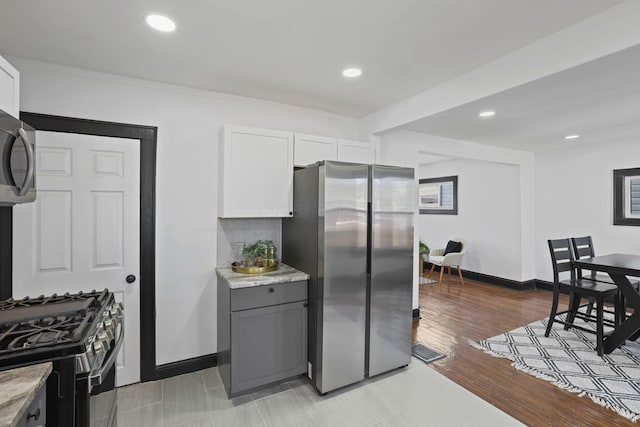 kitchen featuring visible vents, range with gas stovetop, backsplash, freestanding refrigerator, and baseboards