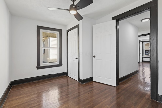 unfurnished bedroom with a closet, ceiling fan, baseboards, and dark wood-style flooring