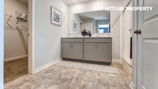 full bathroom with a shower stall, a walk in closet, baseboards, double vanity, and a sink