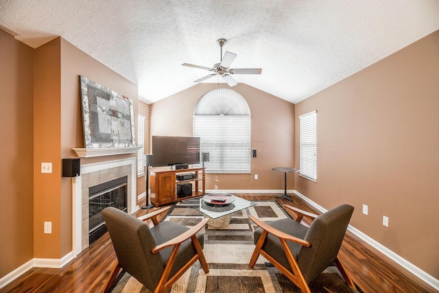 living area featuring a ceiling fan, lofted ceiling, dark wood-style floors, and a tile fireplace